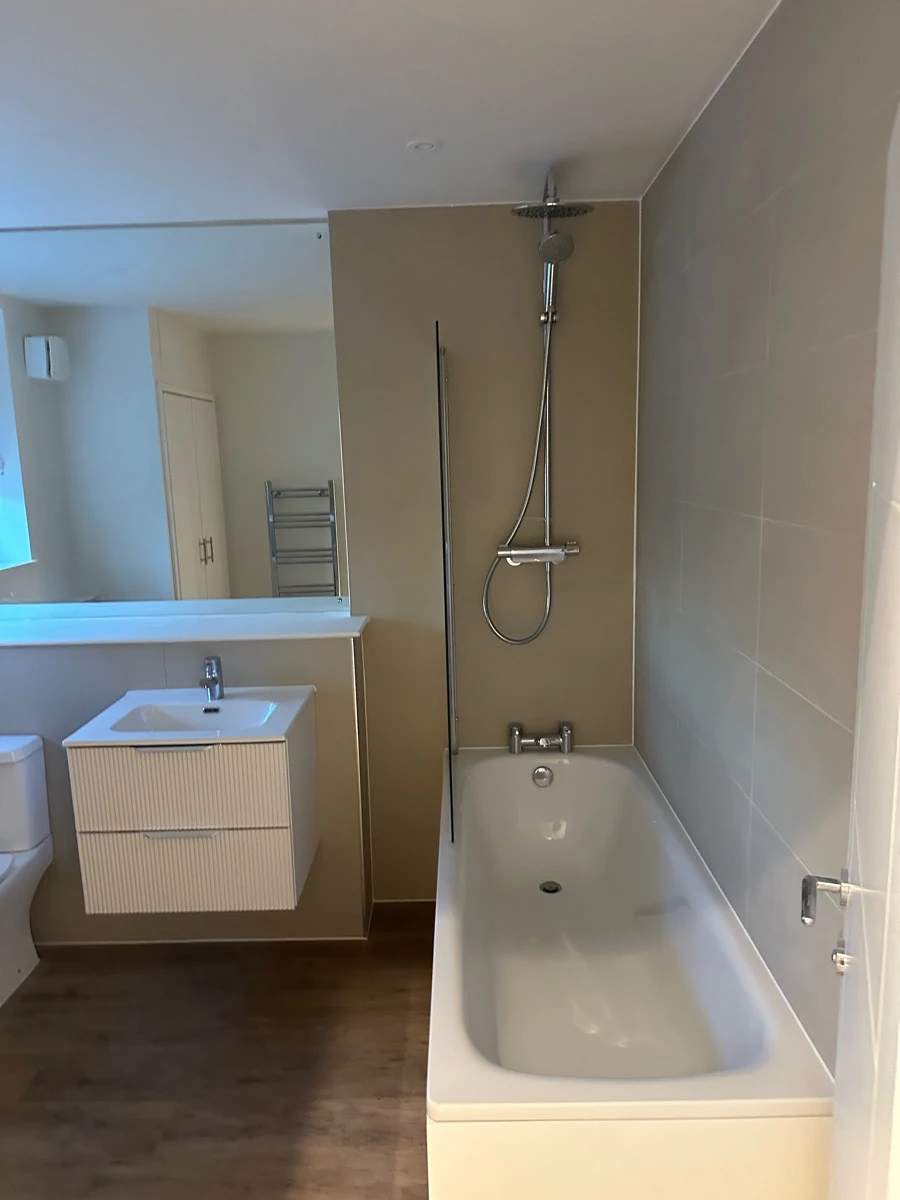 Refurbished bathroom with a wall-hung vanity, mirror and bath with overhead shower.