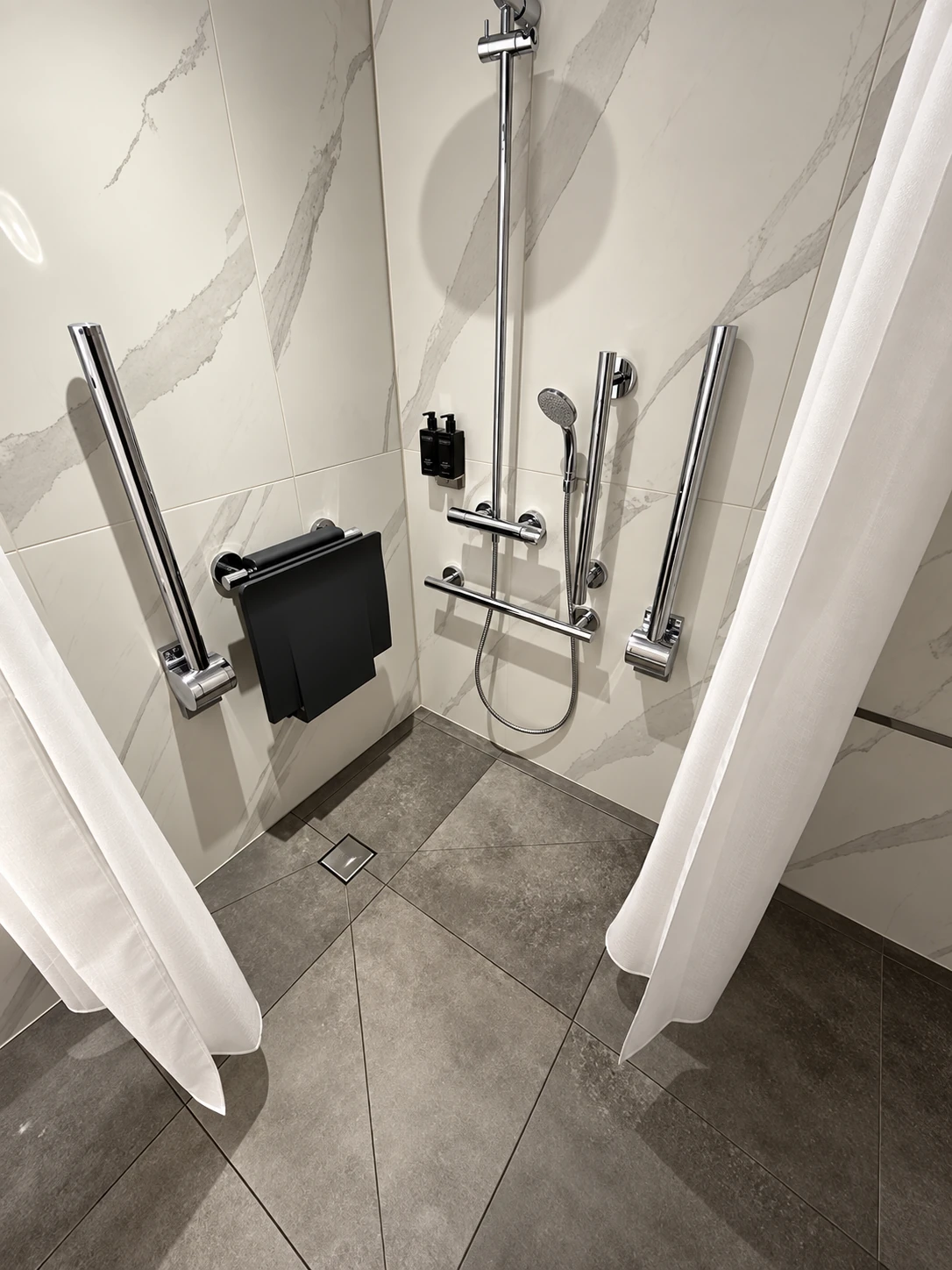 Completed accessible shower room with grab rails, a wall-mounted shower seat and a level-access floor drain